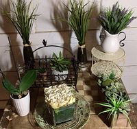 Showing arrangement of artificial plants in various vases, metal basket and decorative items on table