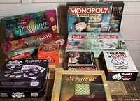 Photo showing multiple boxed board games including Monopoly Ultimate Banking, Monopoly classic, Scrabble editions, Pop Trivia, Texas Hold Em, Spider Solitaire, and You Are A Liar games arranged together.