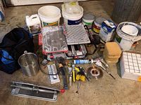 Full lot overview showing wet tile saw, manual tile cutter, buckets, tools, and supplies arranged on floor.