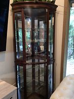 Front view of cherry wood curio cabinet showing curved glass panes and mirrored back with interior shelves.