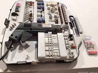 Complete view of Dremel rotary tool and various attachments inside a worn white case with broken lid.