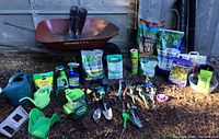 Full lot view showing wheelbarrow, gardening boots, watering cans, fertilizers, garden tools and accessories spread on ground