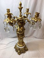 Front view of gold ornate candelabra with three goddess figures and hanging crystal prisms
