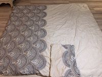 Cream and indigo printed comforter with white background and scalloped pattern visible, laid flat on floor.