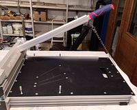 Side view of the floor cutter showing the arm with ergonomic handle and chain support on a black metal platform with metal frame.