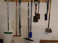 Photo showing various long handled cleaning tools including brooms, ash scoops, and a cobweb duster mounted on a wall