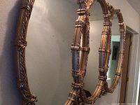 Side angle showing the depth and detailed carving of the three connected oval mirrors' gold-toned plastic frames.