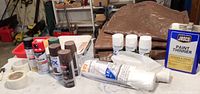 Cans of paint thinner and assorted spray paints along with brown tarps folded in background