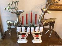Photo of the full set including two silver chrome reindeer, two small white painted wooden reindeer candleholders, and vintage electric candleholder with red candles and greenery.