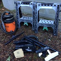 Photo showing two grey plastic sawhorses and all vacuum attachments on the ground beside them, including hoses and nozzles.