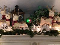 Overall display of seven straw-covered reindeer on greenery garland with clear bead string lights, black lantern behind and star shower light casting light effects