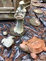 Outdoor setup showing the St Francis statue holding a bird and bird bath, alongside the large turtle and two frogs on ground covered with leaves and black outdoor fabric.
