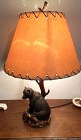 Lamp with bear-shaped base, brown lampshade with leather lacing and branch-style stand on wooden table
