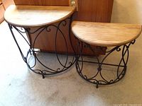 Photo showing two small curved half-moon shaped tables side-by-side with wood tops and black metal ornamental bases.