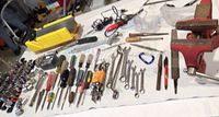 Photo showing a variety of hand tools laid out including screwdrivers with different heads, open-end wrenches of varying sizes, socket wrench parts, and a few long handled tools.