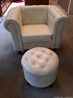 Front view of white faux leather armchair with button tufted backrest and rolled arms, with round ottoman in front
