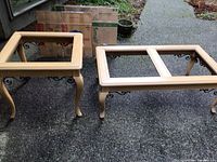 View of one square side table and one rectangular coffee table without the glass tops on top, showing wood frames and metal trim with scroll detailing on legs.