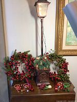 Full view of the street lamp with two berry wreaths, doorknob decorations with jingle bells, and poinsettia night light arranged on a table.