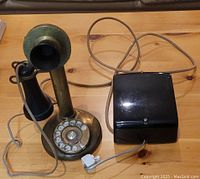 Full view of the antique brass candlestick rotary phone placed on a wooden surface accompanied by a black box adapter and connecting cords.