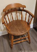 Photo of one wooden captain's chair showing rounded seat, spindle backrest, curved arms, and wood finish.
