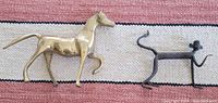 Photo showing a polished brass horse sculpture and a dark metal monkey sculpture placed on a light and dark striped textured mat.