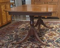 Side angle view of Duncan Phyfe dining table showing double pedestal bases and curved legs on patterned carpet.