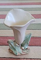 Full view of the McCoy vase shaped like a Calla lily flower with green leaves at the base, shown on striped carpet background.