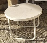 Close-up image of the small round white metal patio table showing tubular legs and solid white top.