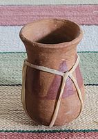 Small unglazed earthenware vase with rough finish, tied with string around center.