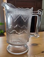 Front side view of the pressed glass water jug showing the spout, handle, and textured geometric pattern.