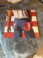 Front cover showing Bruce Springsteen's backside wearing jeans, white t-shirt, red cap in back pocket against USA flag background