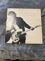 Full front view of the Born to Run album cover showing Bruce Springsteen playing guitar with white background and visible wear on the album cover.