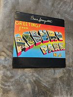 Front cover of Bruce Springsteen Greetings From Asbury Park N.J. vinyl album showing colorful lettering and artist name