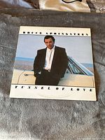 Front cover of Bruce Springsteen Tunnel of Love vinyl album showing artist standing against a car by the beach.