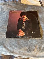 Vinyl LP cover showing Burton Cummings seated with hands clasped, wearing a floral patterned shirt and pinstriped jacket. The cover has visible wear and creasing.