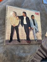 Front cover of FORE! album by Huey Lewis and The News depicting three band members against a wall.