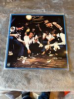 Front cover of Little River Band "Time Exposure" vinyl album showing photo of band members and dog with glass shards on floor.