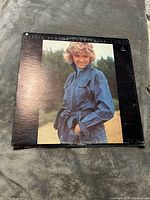 Front album cover with Olivia Newton-John in a denim jacket, smiling outdoors, background natural greenery.