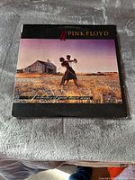 Front cover of Pink Floyd LP titled 'A Collection of Great Dance Songs' showing a person dancing in a field with a house and sky background.