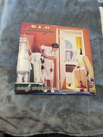 Front cover of REO Speedwagon Good Trouble vinyl album showing the illustrated scene of a woman and man near a door.