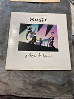 Front cover of the white album jacket featuring stylized graphic of band members and album title 'Rush a show of hands'