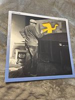 Front cover of the Supertramp Free as a Bird vinyl album showing an elderly man painting a yellow bird on a piano.