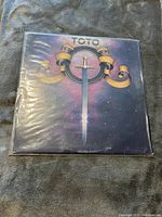 Front cover of Toto vinyl album showing sword and ribbon emblem with band name