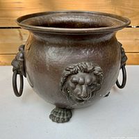 Front view of copper planter showing lion head motif, ring handle and paw feet
