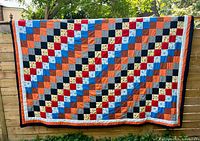Full view of quilt hung outdoors showing entire multicolour patchwork pattern and borders