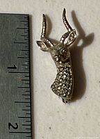 Front view of sterling silver deer head brooch beside ruler showing size
