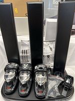 Three black stands and three bottle dispensers with chrome levers arranged next to each other. Mounting hardware including screws and clamps placed beside the stands.