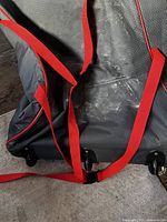 Close-up showing the bottom of the large black storage bag with red carrying straps and wheels for mobility, some dust visible.