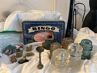 Photo shows glass insulators, Wade animal figurines, old hammered spoon, ice wine bottles/vases, and bingo game box