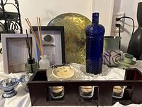 Wide view of decor items including wooden candle holder with three glass cups, blue bottle, gold decorative plate, aroma diffuser bottles, pottery dishes, and framed art pieces.